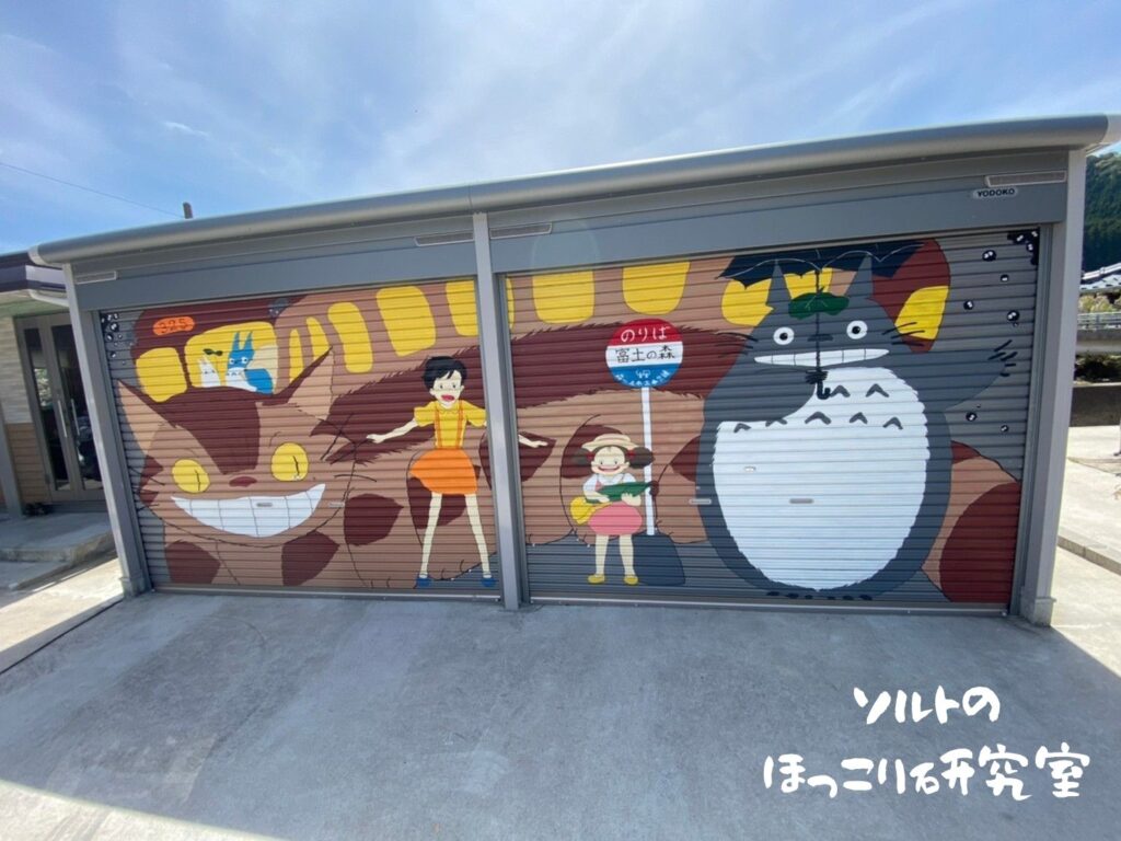 富土のトトロのガレージに、ネコバス、傘を持ったトトロ、サツキ、メイの絵が描かれている様子。